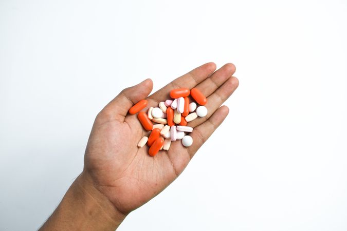 Hand holding variety of colorful medication and vitamins with plain background