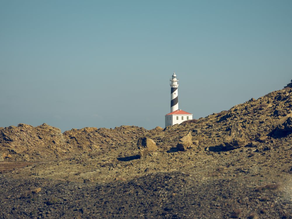 Lighthouse tower with house behind rough rocky formations