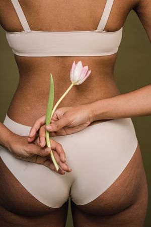 Back view of Black woman in bra and panty holding lotus flower