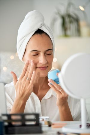 Relaxed woman with closed eyes applying smoothing face cream