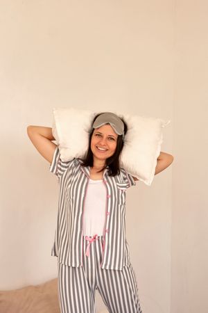 Woman smiling, holding pillows while standing in bed.