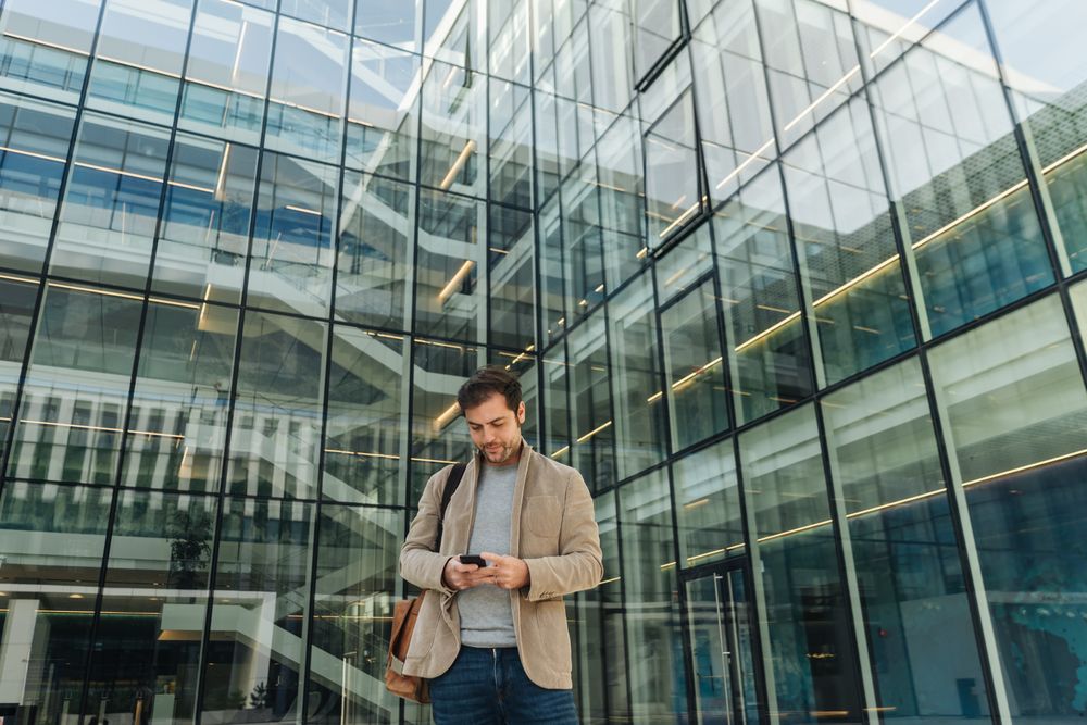 Smiling entrepreneur using smartphone outside office building
