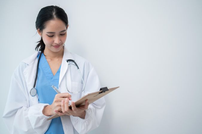 Doctor standing in bright hospital room writing in clipboard with copy space