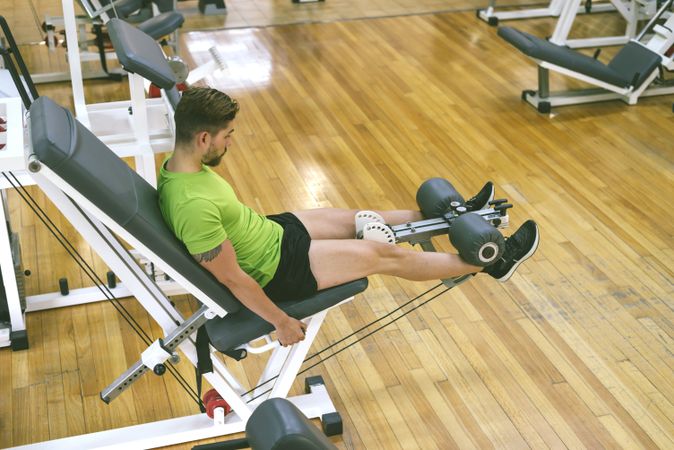 Looking down at muscular male in green t-shirt working out using leg extension machine, copy space