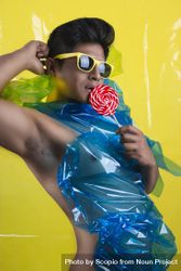 Sexy bare-chested man with blue plastic on chest wearing yellow framed sunglasses holding lollipop 47Erl0
