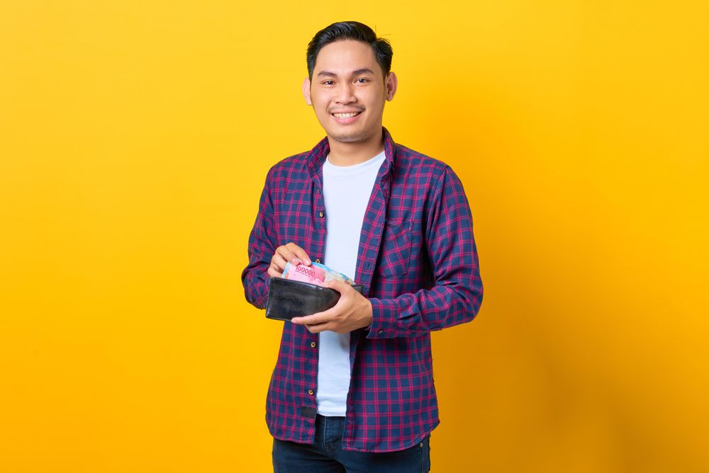 Smiling man taking cash out of his wallet