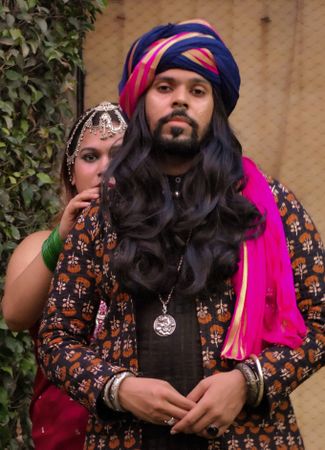 Indian man with long hair wearing a turban and woman standing right behind him