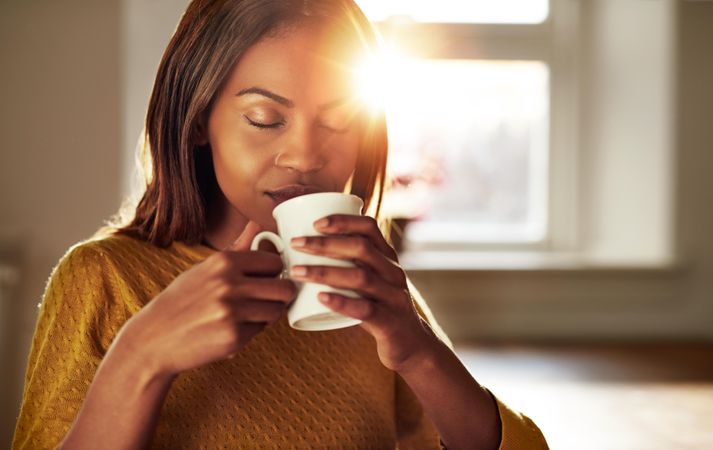 Woman sips from coffee mug in sunny room