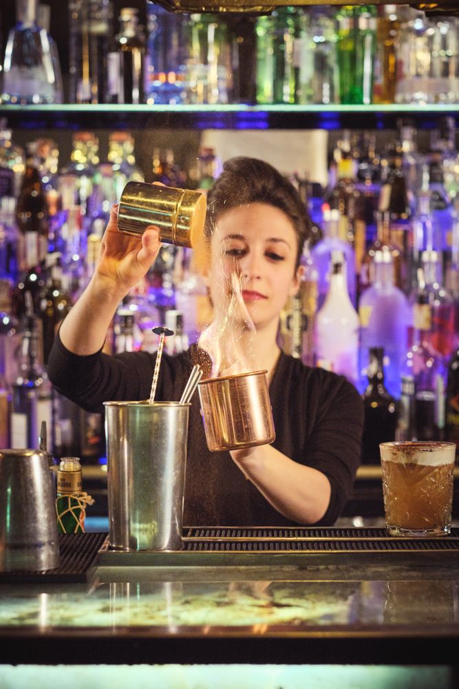 Professional female barkeeper adding salt into flaming cocktail