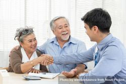 Smiling Asian couple making purchase with mature woman shaking hands with real estate agent 4ZQx95