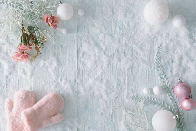 Wooden table background with snow and flowers and festive pink decorations and mittens