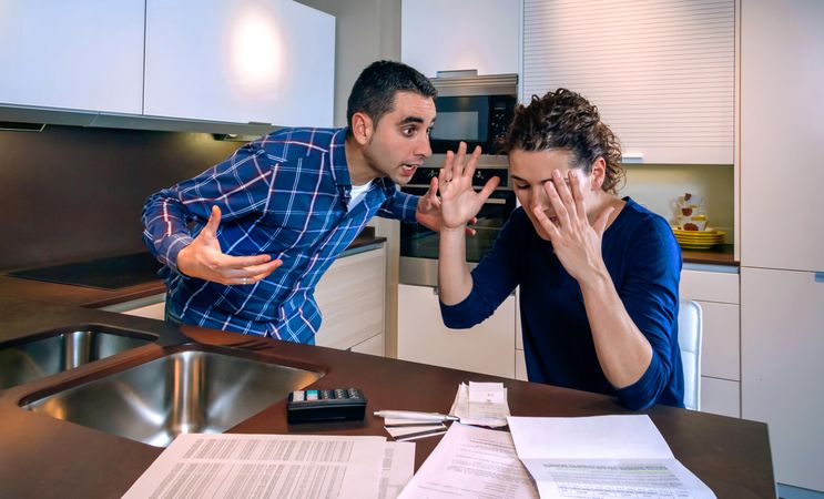 Couple arguing in kitchen with bills on counter