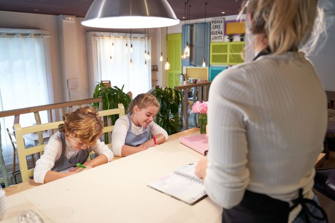 Happy children taking notes before cooking with anonymous mom