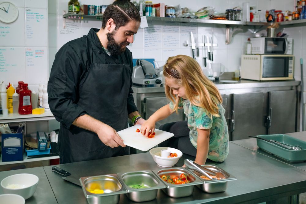 Chef teaching little girl how to prepare healthy poke bowl in a professional kitchen