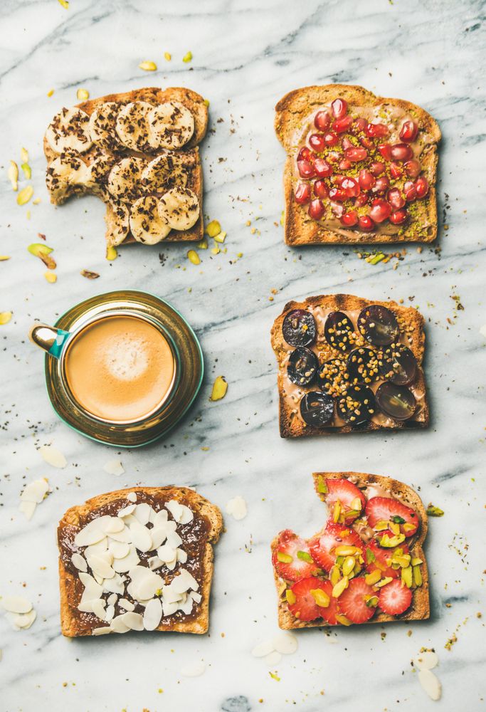 Toasts with bites taken out, with different fresh fruit toppings on marble counter, with coffee