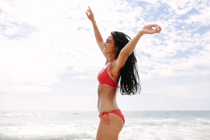 Profile shot of playful woman dancing in swimsuit on beach