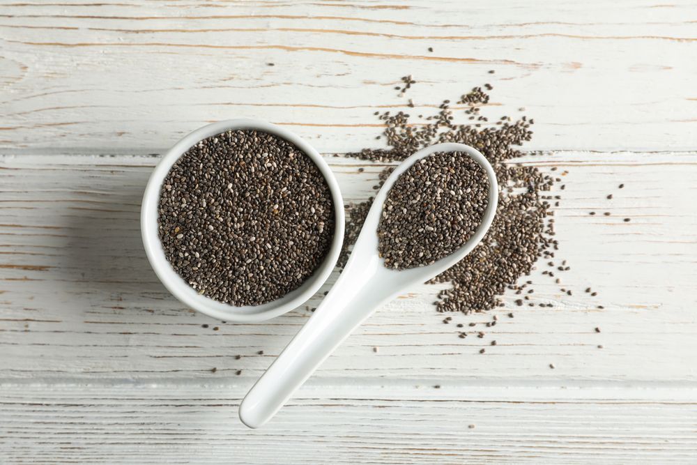Ceramic sauce boat and spoon with chia on wooden background, top view