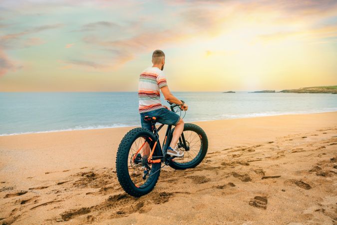 White male sitting on bicycle and looking ahead at beautiful view along the coast