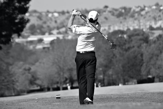 Back view of man playing golf in grayscale