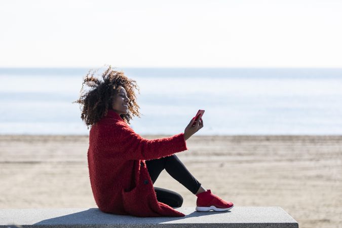 Side view of female taking picture on smart phone on bench near the sea