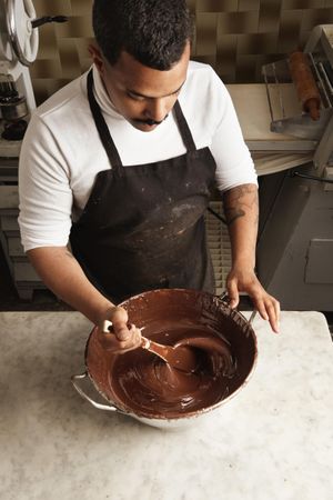 Above shot of man in apron stirring melted chocolate in kitchen