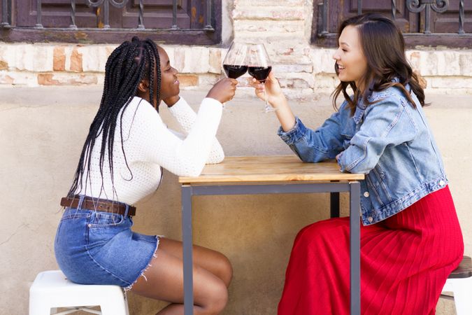 Female friends toasting red wine at an outdoor table at a restaurant