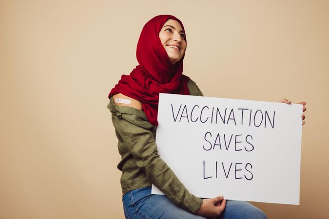 Female wearing hijab holding a banner of "vaccination saves lives"
