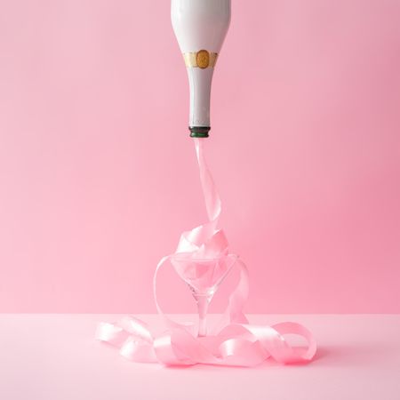 Champagne bottle with pink party ribbon on pink background