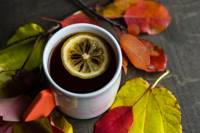 Top view of hot beverage with lemon slice in a mug surrounded by fall leaves