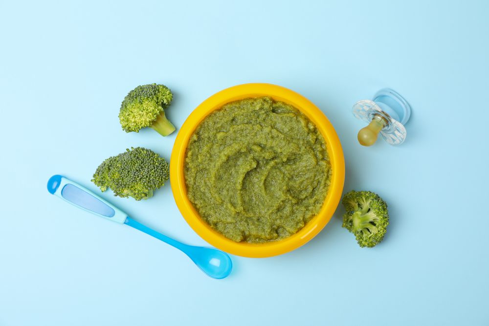 Bowl with broccoli puree on blue background, top view