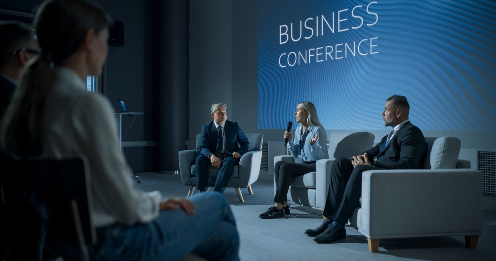 International Business Conference: Female Tech CEO Talking With Male Host In Front Of Audience Of Diverse Attendees.
