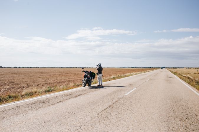 Man on side of a vast rural road with motorcycle