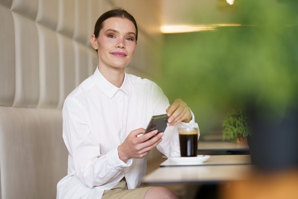 Successful elegant woman smiling while using smartphone in a cafeteria