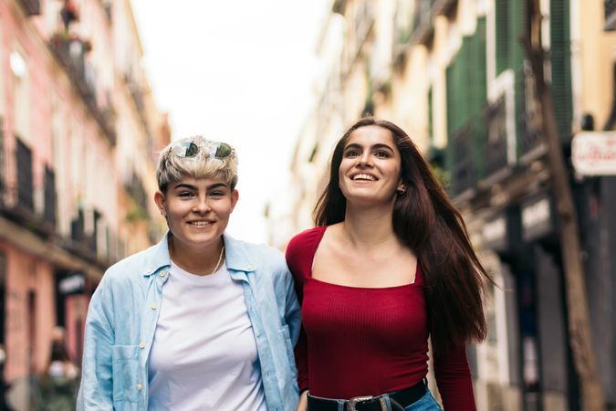 two happy women walking and smiling on a street, front view
