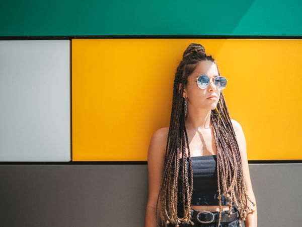 Charming teenage girl with dreadlocks in sunglasses nearby colorful wall