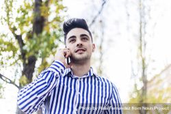 Portrait of man standing in striped shirt speaking on phone outside bDjQYJ