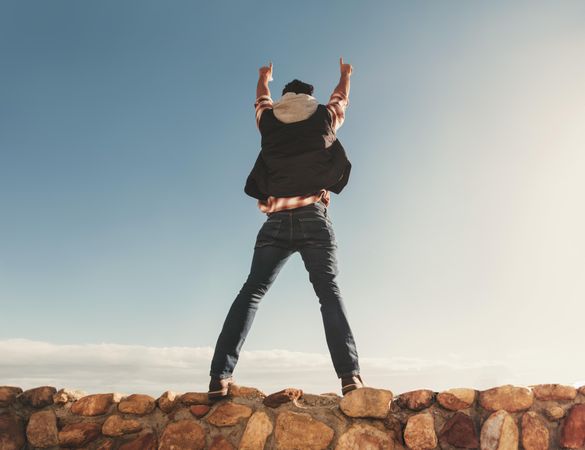 Man standing on rock wall with arms in the air