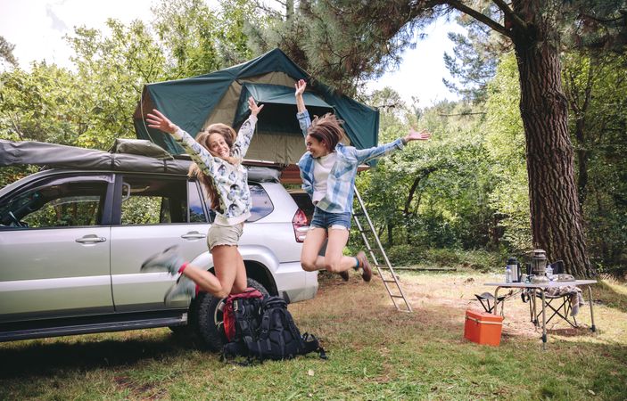 Women friends jumping in campsite into the forest