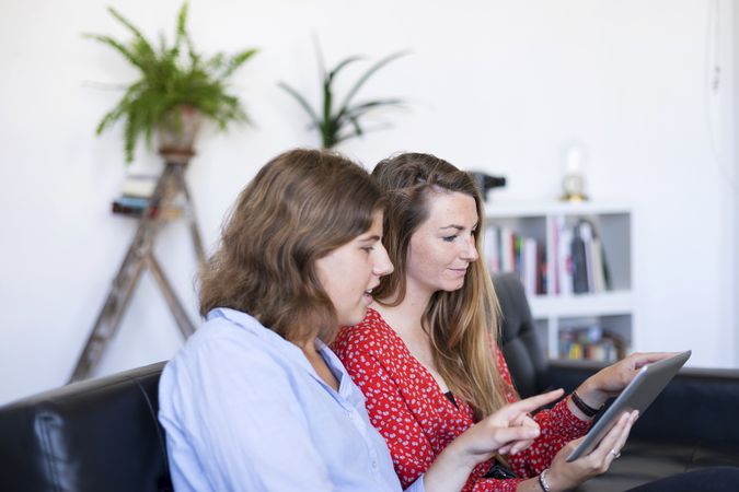 Two young women at home sitting on sofa using digital tablet