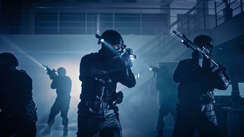 Masked Squad of Armed SWAT Police Officers Stand in Dark Seized Office Building with Desks and Computers.