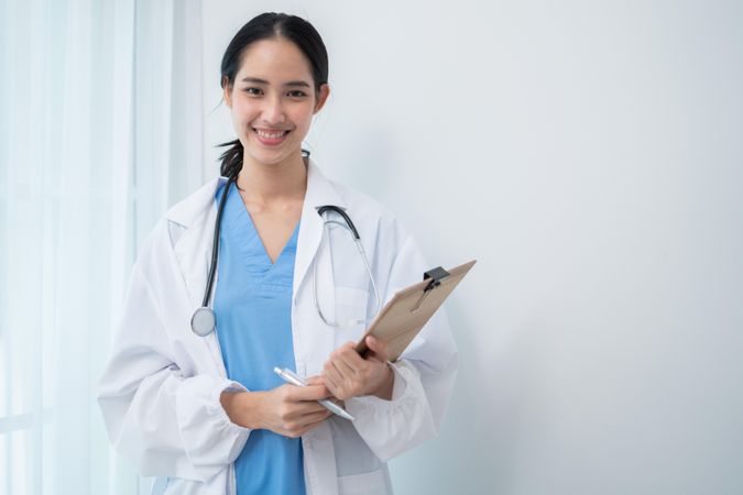 Smiling Asian doctor standing in light hospital room with copy space
