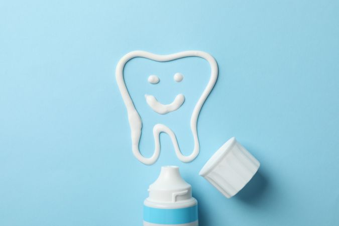 Tooth made of toothpaste and tube on blue background, top view
