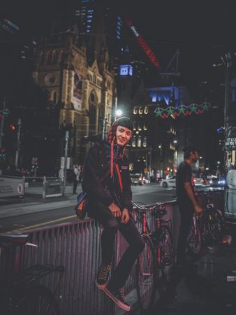 Man in leather jacket sitting on a rail on street during night time