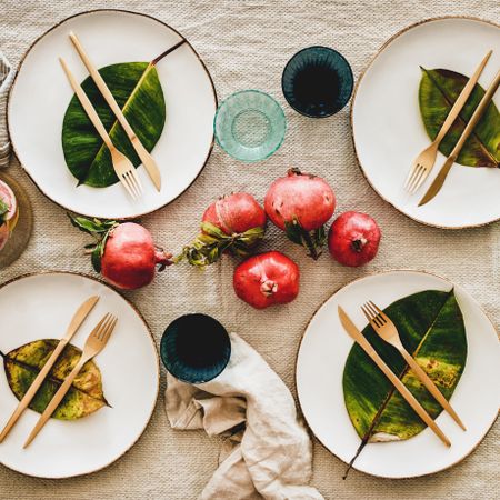 Fresh table setting on brown table cloth, leaves on bright plates, pomegranate, square crop
