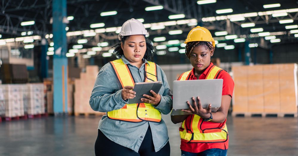 Female co workers discussing work together in distribution center, wide