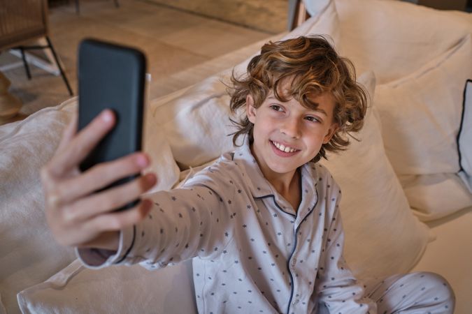 Positive boy in pajama taking selfie on smartphone