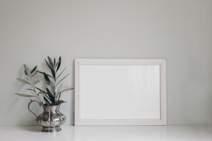 Horizontal wooden picture photo frame on table next to olive twig in vintage silver vase