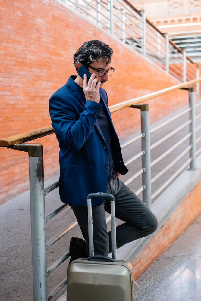 Older man standing with baggage and talking on smartphone