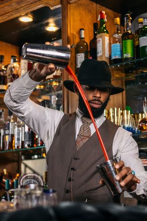 stylish Black bartender preparing a cocktail in a shaker in a traditional cocktail bar