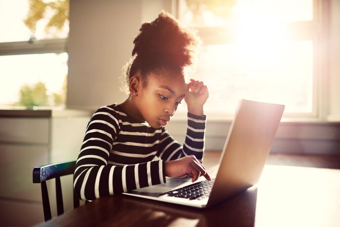 Serious Black girl works on laptop in sunny kitchen